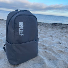 Indlæs billede til gallerivisning Bæredygtig grå rygsæk af genanvendt plastik til kvinder og mænd. Rygsækken står oprejst på en strand.