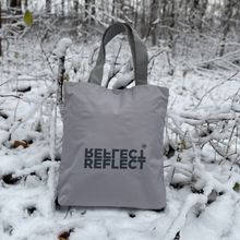 Indlæs billede til gallerivisning Lysegrå shopping bag med mørkegråt logo. Den bæredygtige tote bag er placeret i en skov med et fint lag sne.
