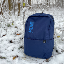 Indlæs billede til gallerivisning Bæredygtig blå rygsæk af 100 % genanvendt plastik til kvinder, mænd og børn. Rygsækken står oprejst i en snefyldt skov.

