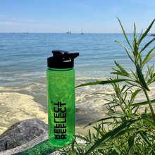 Indlæs billede til gallerivisning Grøn drikkedunk af genbrugsplast. Den har et flip-top låg, der let kan lukkes og åbnes. Vandflasken har plads til 700 ml. væske. I baggrunden ses havet på en solskinsdag.
